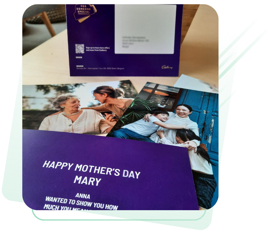 A set of printed photo cards and envelopes with personalized messages and family images, including one reading “Happy Mother’s Day Mary” in white text on a purple background. Branded Cadbury packaging is visible in the background.
